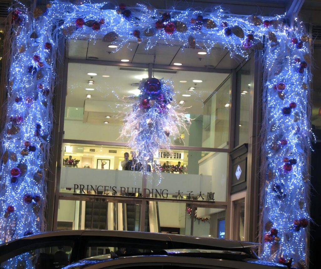 Entrée d'un bâtiment commercial avec guirlande de Noël, cadre lumineux et centre de table festif suspendu.