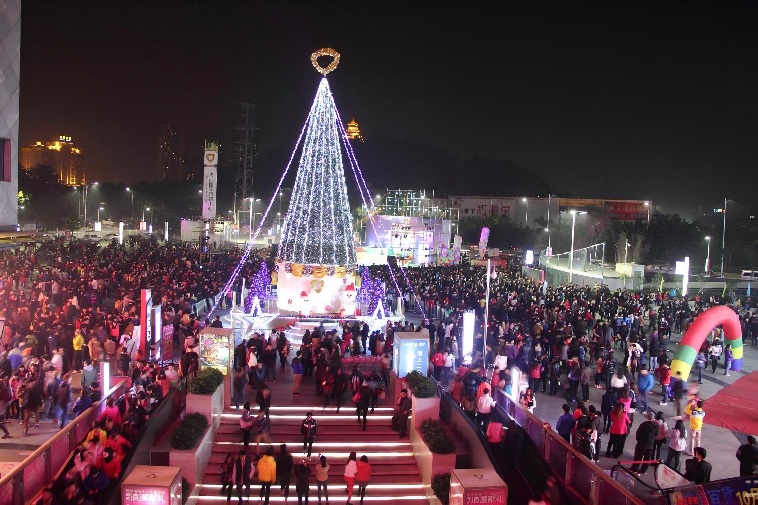 Giant cone-frame commercial Christmas tree in a busy plaza attracting large crowds at night