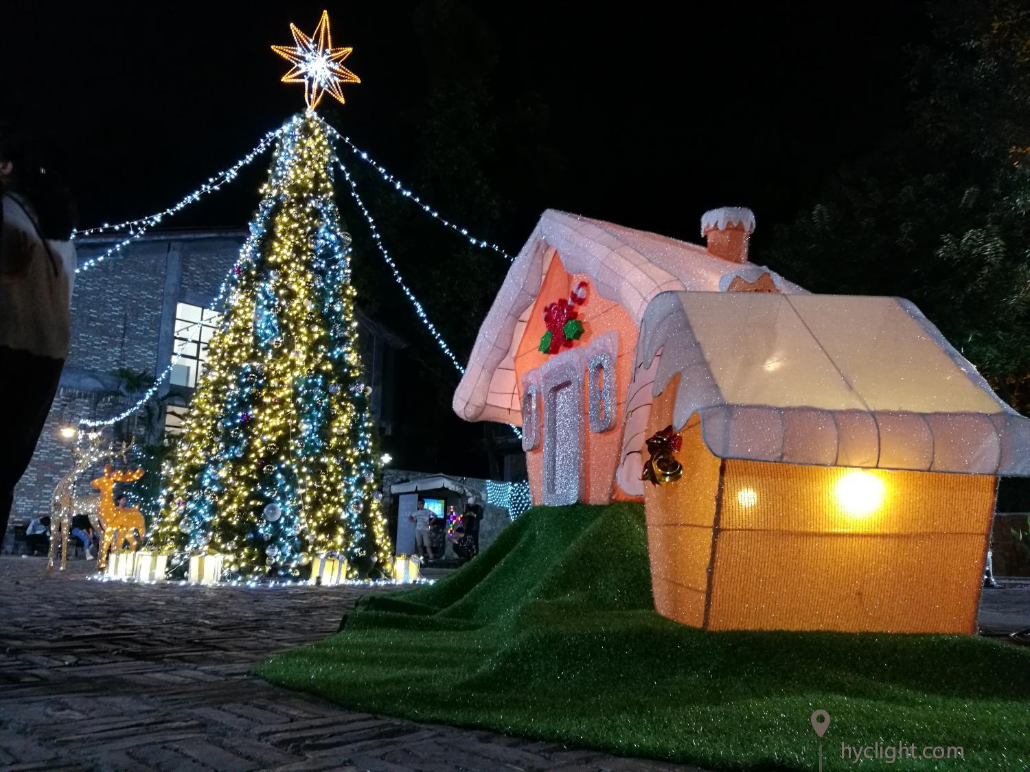 شجرة عيد الميلاد التجارية الكبيرة مع بيت خبز الزنجبيل ومنحوتات الرنة وصناديق الهدايا في مشهد عطلة في الهواء الطلق