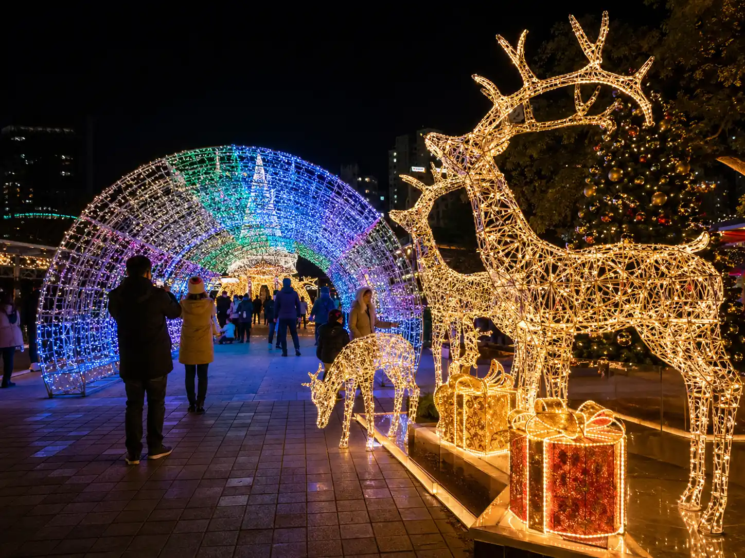 Outdoor park scene with large LED reindeer sculptures, gift boxes, and walk-through Christmas light tunnel