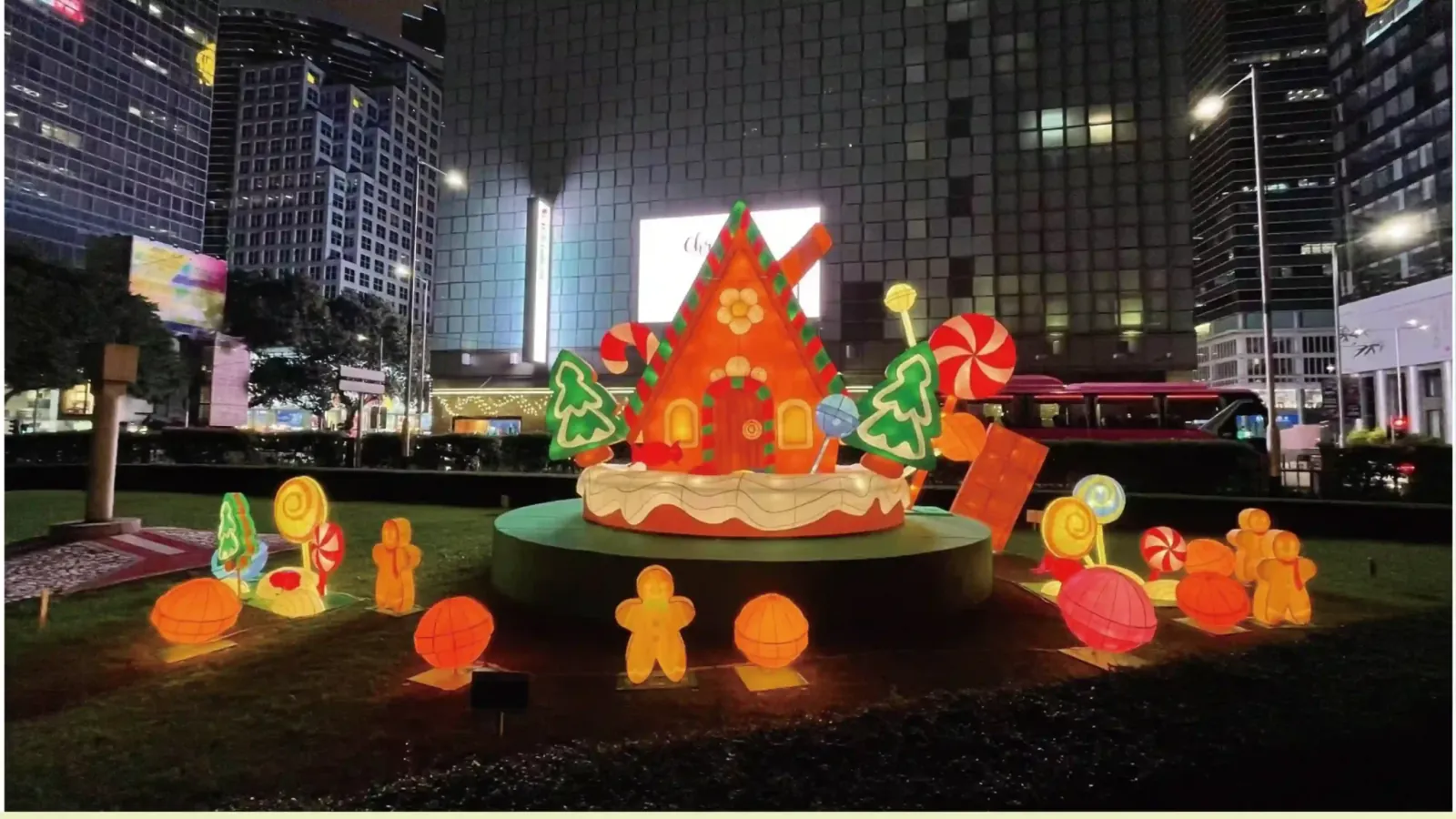 Gingerbread-house display with candy and tree figures on a raised outdoor platform at night
