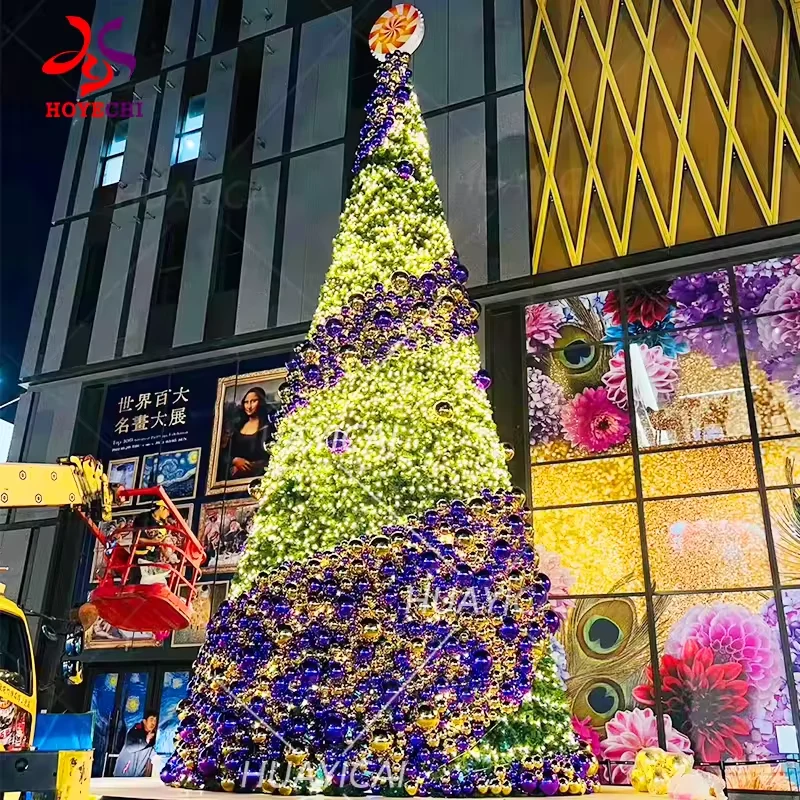 Sapin de Noël commercial violet et doré, orné de larges rangées de décorations, devant un centre commercial