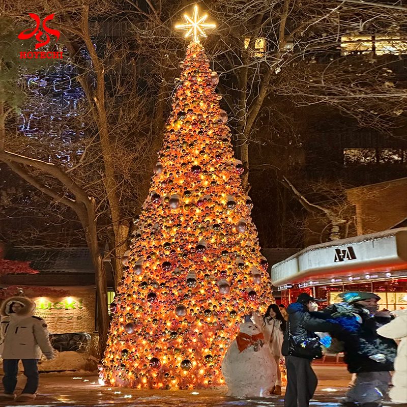 Illuminated outdoor Christmas tree with dense ornament balls for nighttime commercial holiday display
