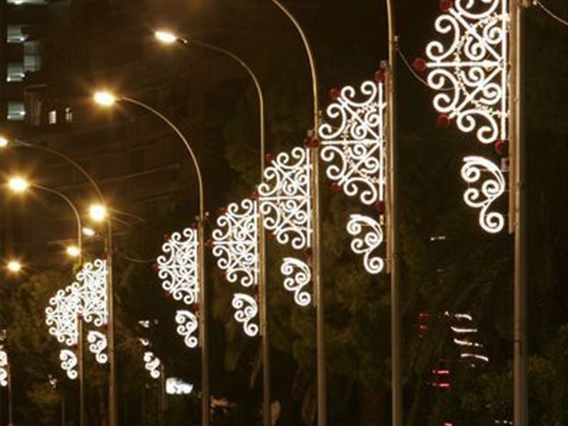 Luces con motivos de postes repetidos instaladas a ambos lados de una amplia vía urbana con un claro ritmo festivo y orden visual
