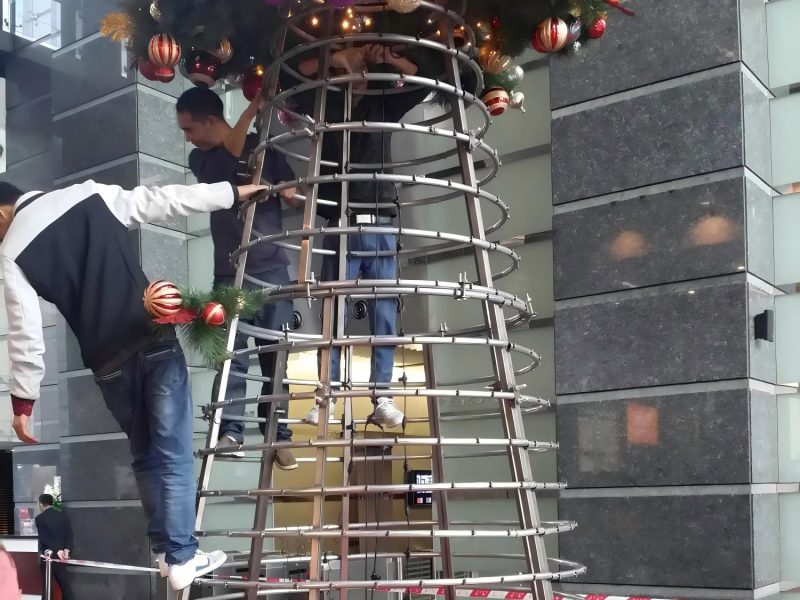 Trabajadores instalando una gran estructura metálica de árbol de Navidad comercial para un proyecto de decoración navideña