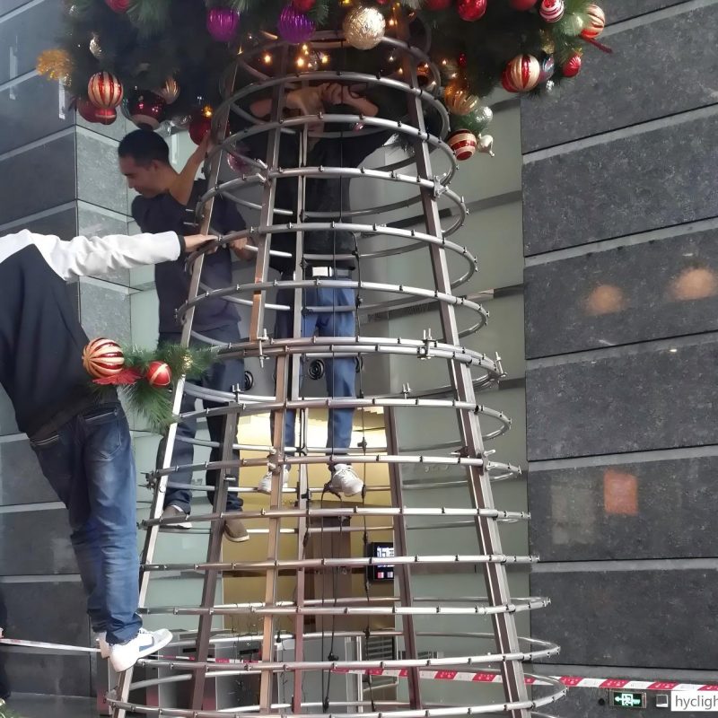 Workers installing a large commercial Christmas tree metal frame structure for a holiday decoration project